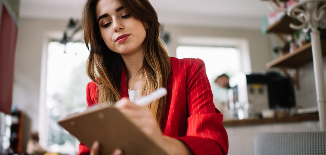 Young woman writing information in notepad